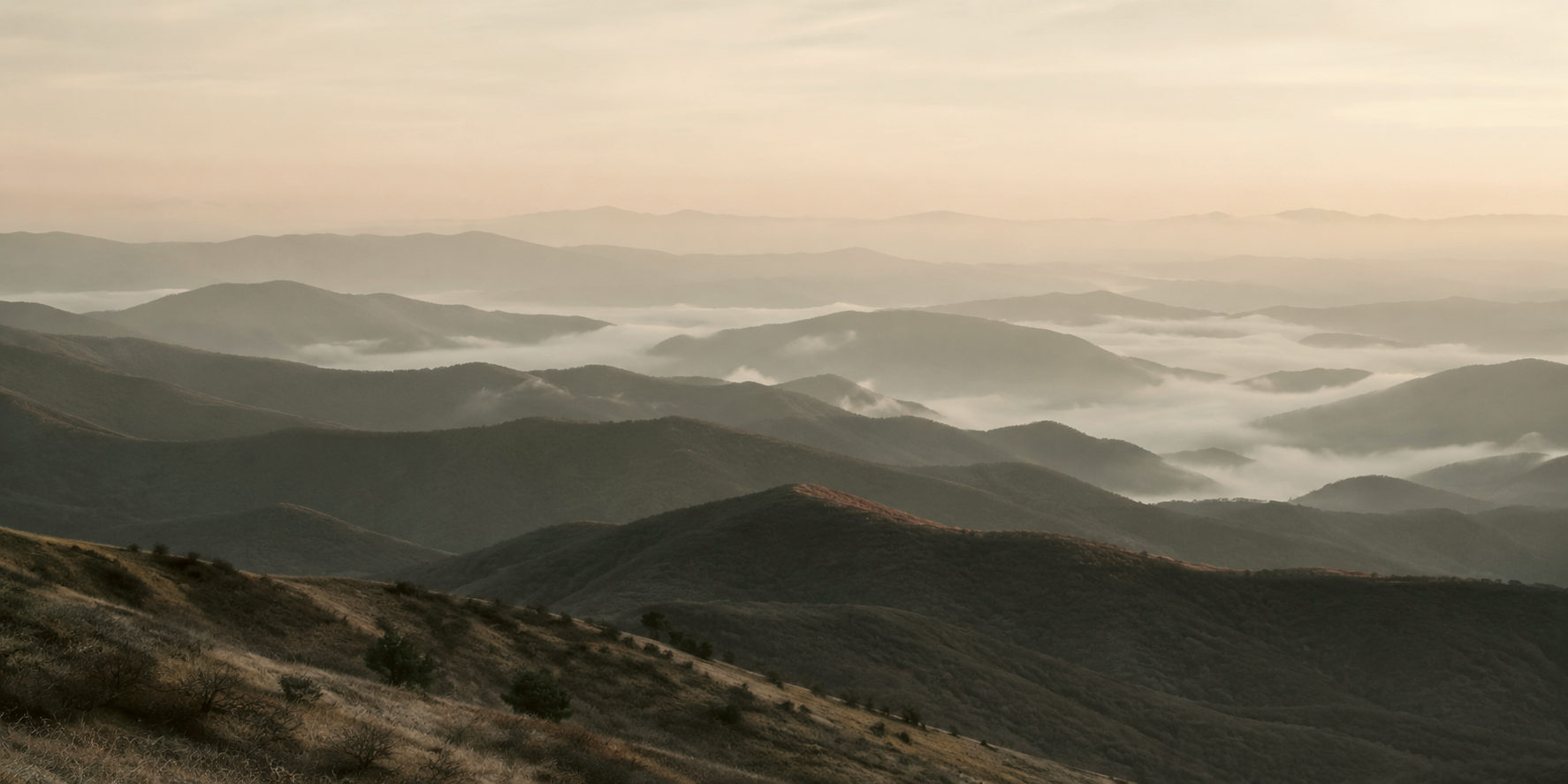Layered ridgelines receding into morning haze, with low cloud settled in the valleys between them.